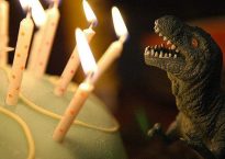 Toy dinosaur facing a cake with lit candles.